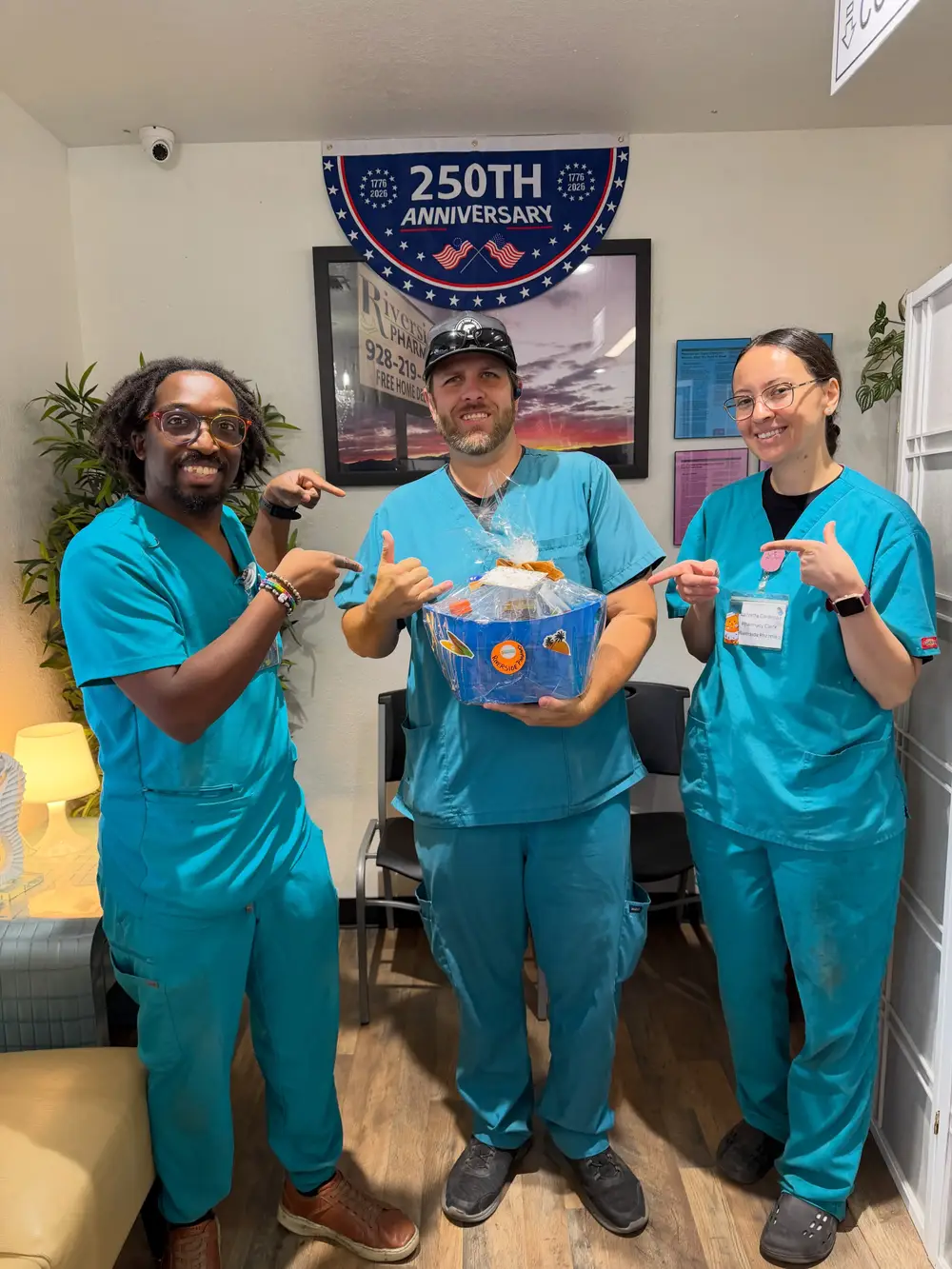 Three Riverside Pharmacy team members in teal scrubs with a gift basket